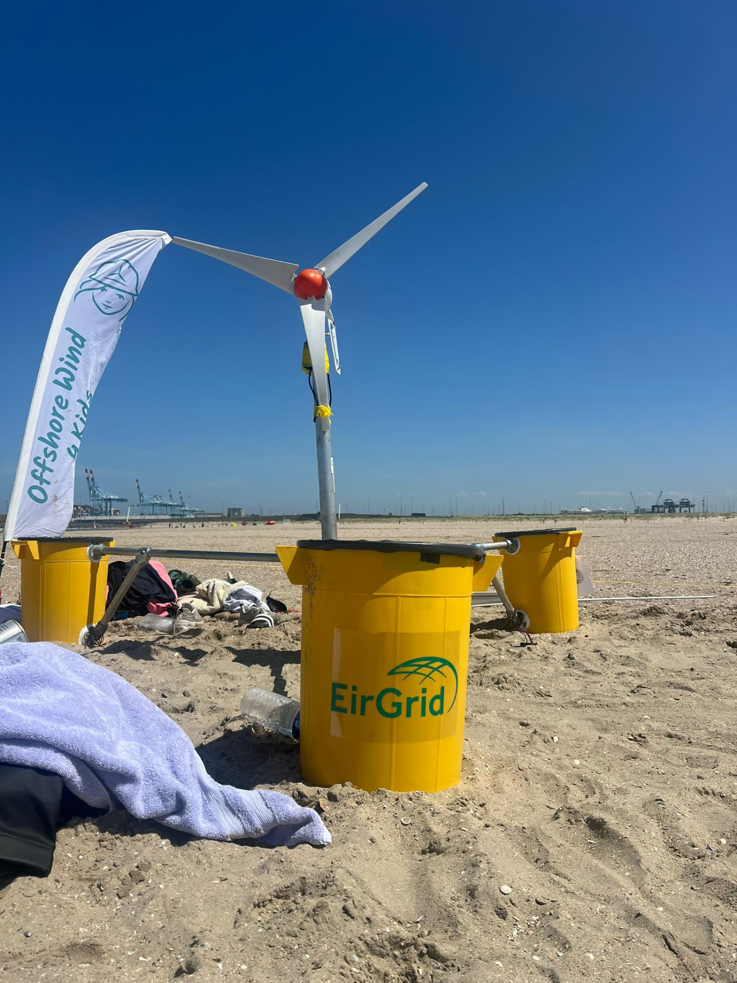 The yellow three-column floating wind platform with its turbine on a sandy beach