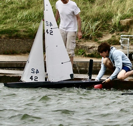 Jeremy crouching at the water's edge launching the SailDrone racing yacht, sails number S4 42