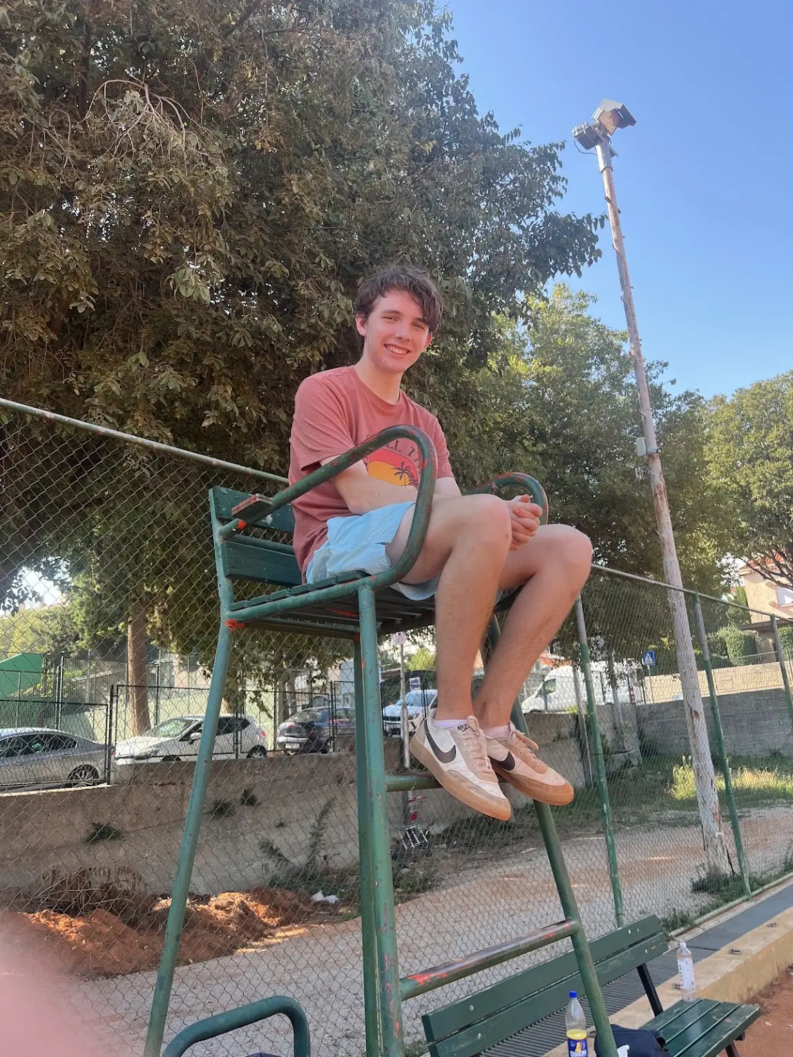 Jeremy smiling while sitting in the referee's chair at a tennis court