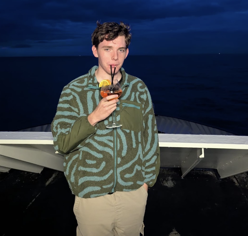 Jeremy in a patterned fleece sipping a spritz on the deck of a boat at night