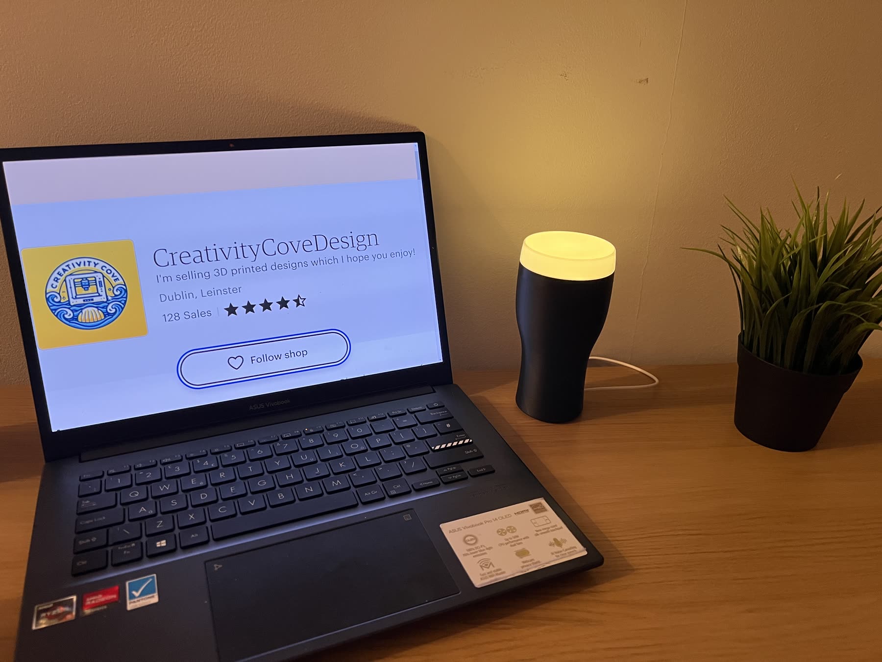The CreativityCoveDesign online shop open on a laptop beside a 3D-printed pint-glass lamp