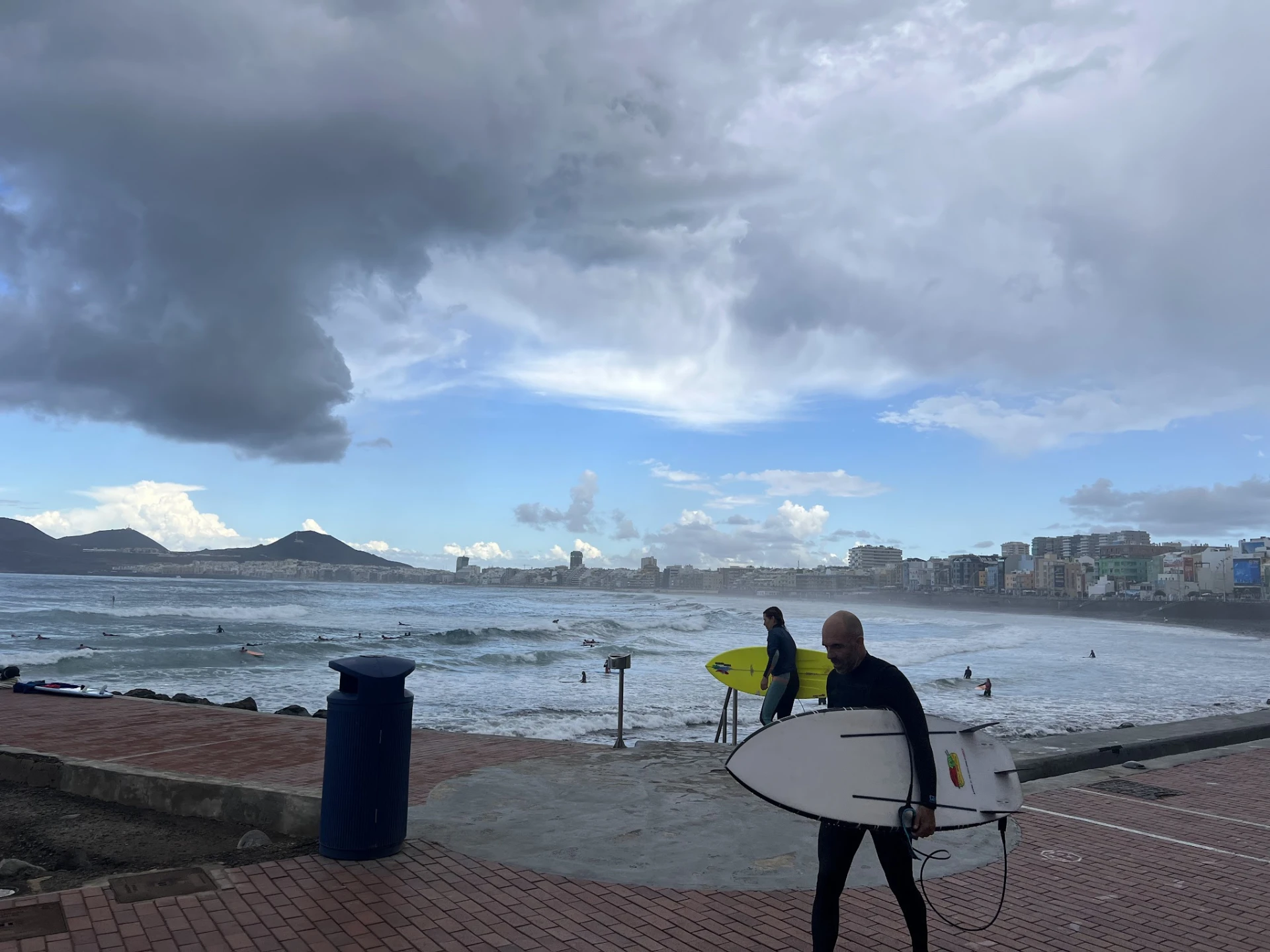 Surfers with their boards on the seafront promenade at Las Palmas, with the city and mountains behind